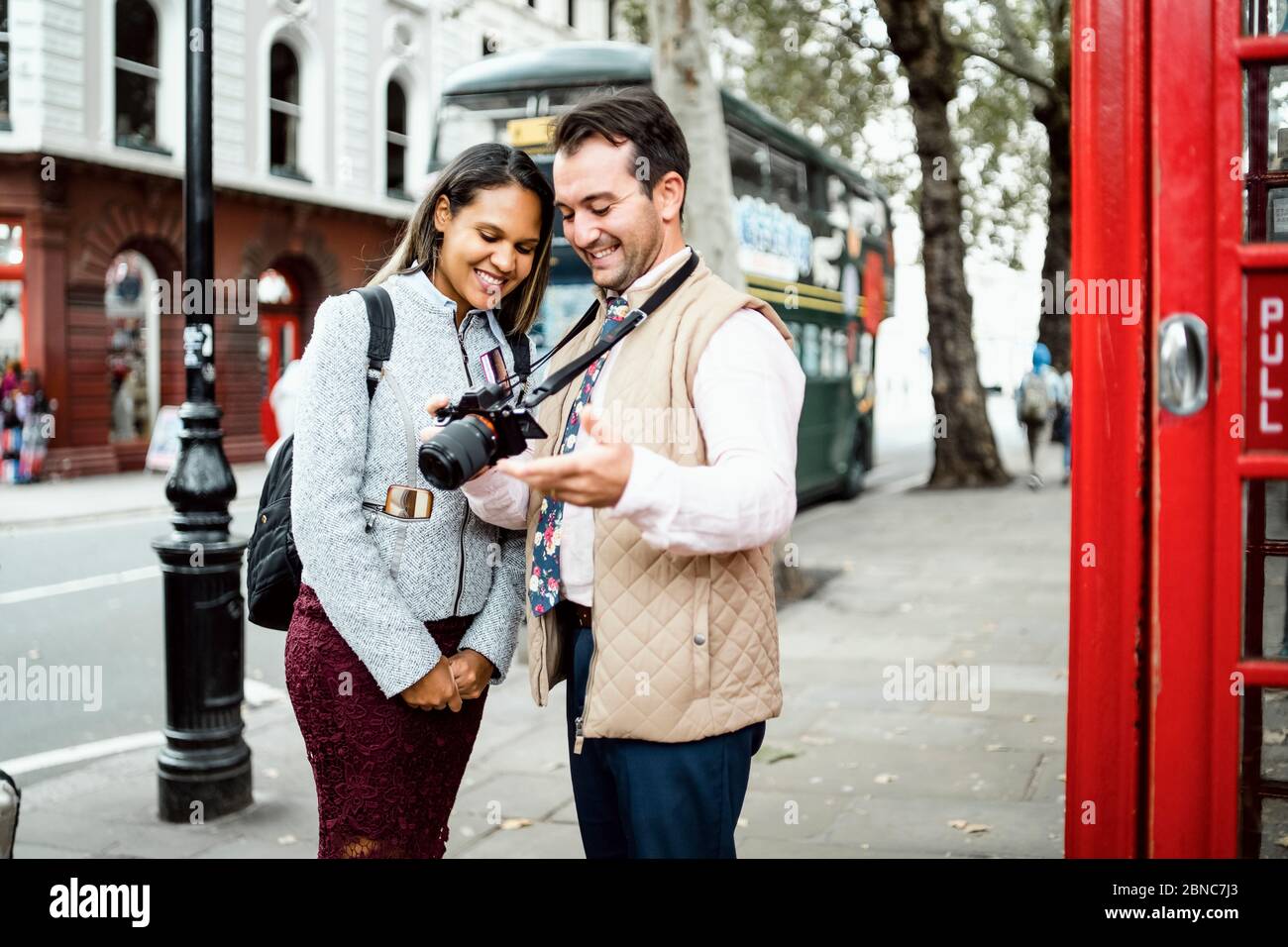Glücklich Reisen Paar Überprüfung Fotos auf ihrer Kamera in London, Großbritannien. Doppeldeckerbus und rote Telefonzelle in einem Rahmen Stockfoto