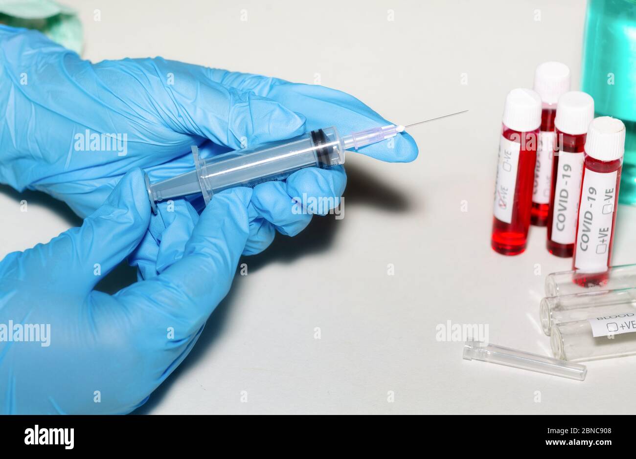 Hände eines Arztes in medizinischen Handschuhen, die eine hypodermische Nadel halten, die Medikamente aus einer Impfstoffflasche mit Blick auf Arzneimittel und Blutproben injiziert Stockfoto