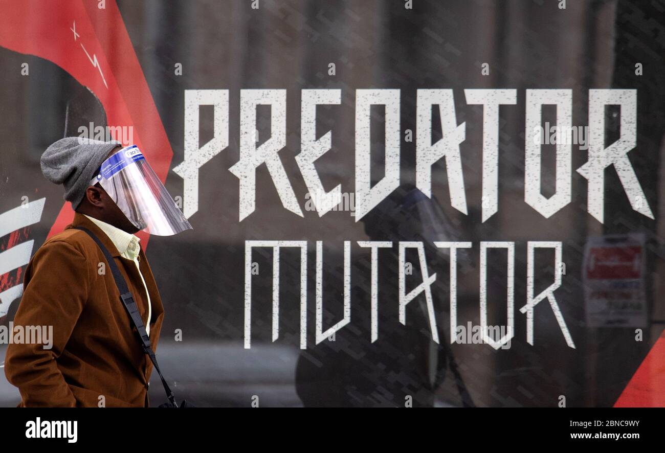 Ein Mann mit einem Gesichtsschild aus Kunststoff geht nach der Ankündigung der Pläne, das Land aus der Blockierung zu bringen, an einer Anzeige mit der Aufschrift "Raubtier-Mutator" in London vorbei. Stockfoto