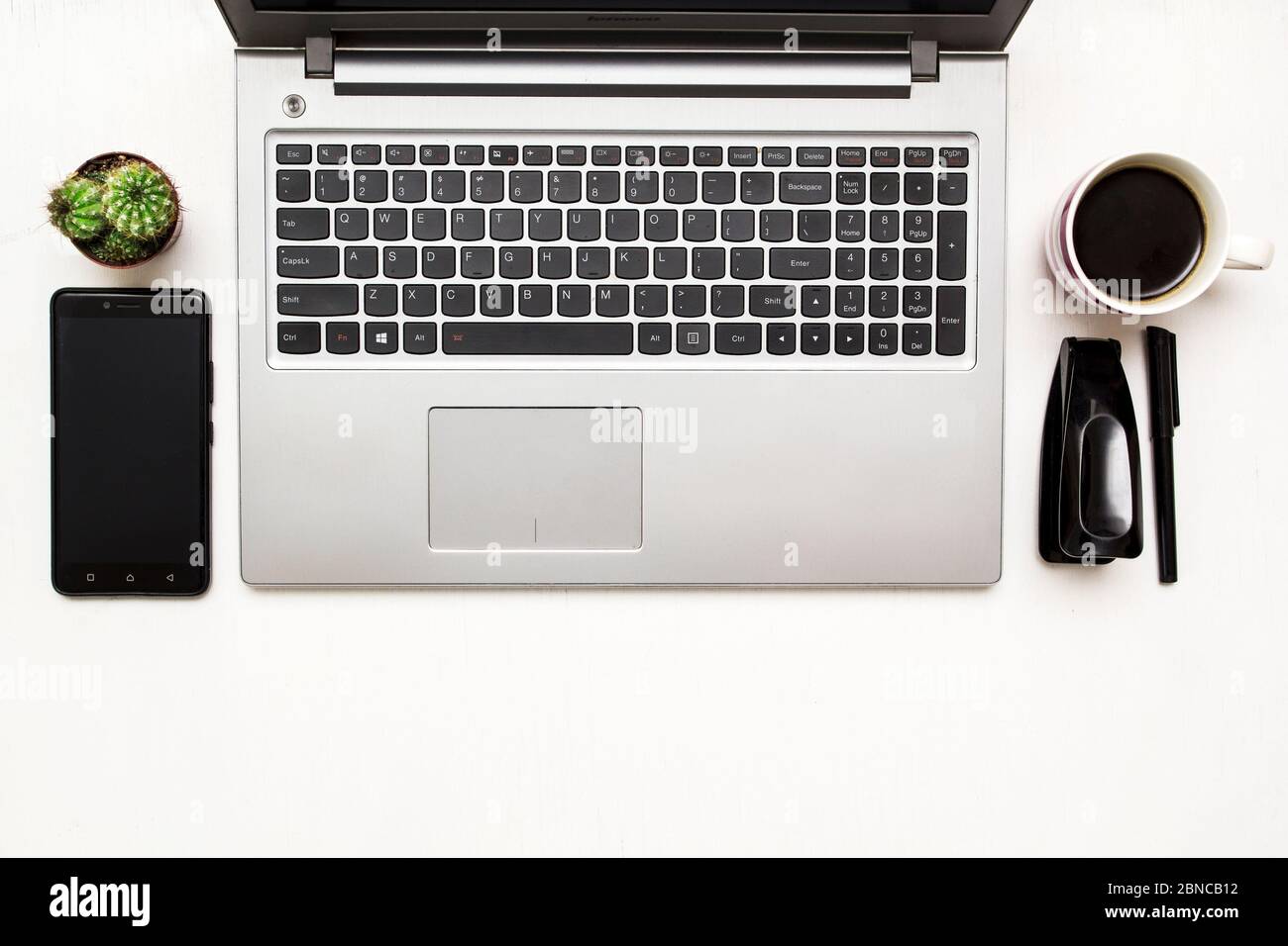 Schreibtisch mit Laptop, Smartphone, stamler und einer Tasse Kaffee und Kaktus. Draufsicht. Stockfoto