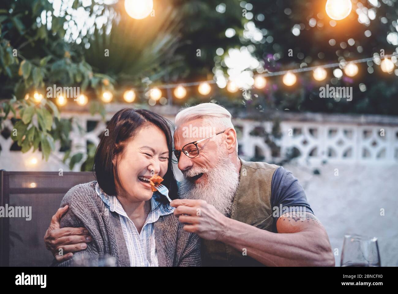 Glücklich Senior Paar Spaß am Abendessen Haus Partei - ältere Menschen mit verschiedenen ethnischen Zugehörigkeit tun ein romantisches Datum für Jubiläum zu feiern Stockfoto