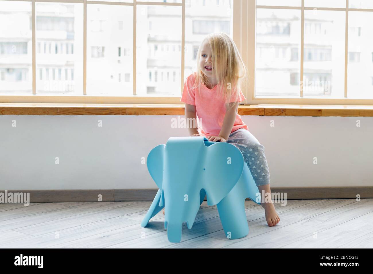 Glücklich kleine blonde Mädchen Reiten auf Elefant Spielzeug im weißen Zimmer Stockfoto