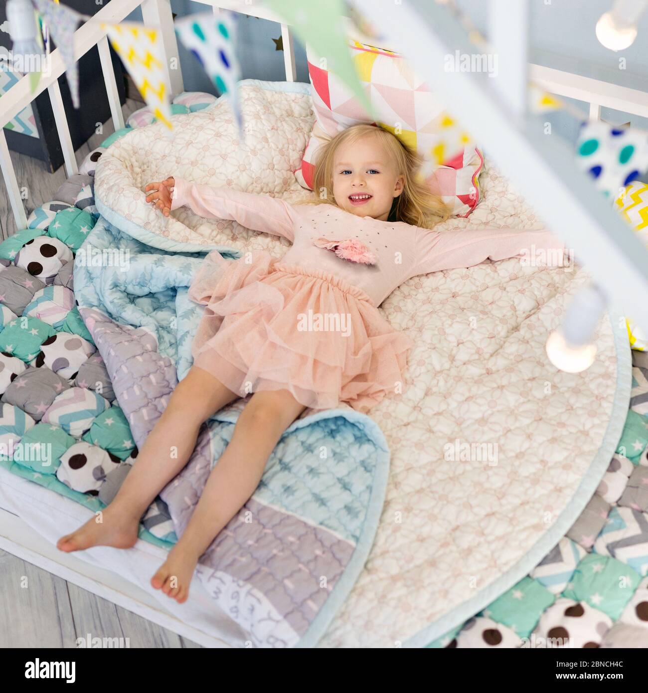 Glückliches Mädchen tragen niedliches Kleid auf gemütlich dekorierten Bett liegen Stockfoto