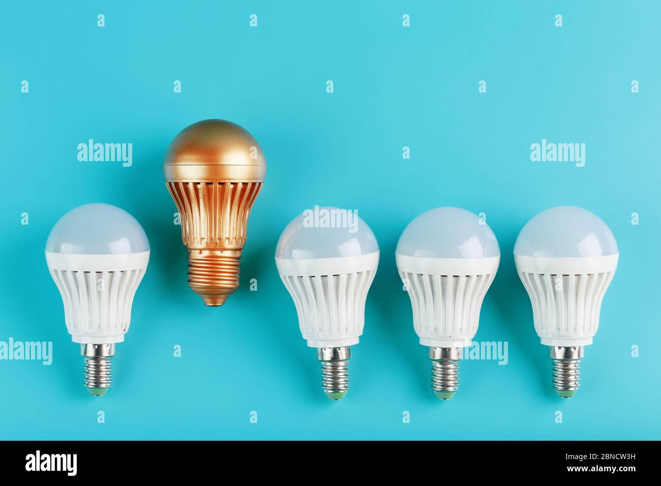 Eine goldene LED-Glühbirne ist höher und hebt sich von einer Reihe von weißen Lampen auf einem blauen Hintergrund. Das Konzept des nicht-Standard-Denkens, Führung und Stockfoto