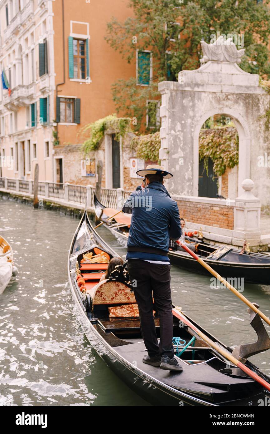 Italien Hochzeit in Venedig. Ein Gondolier rollt ein Brautpaar in einer klassischen Holzgondel entlang eines engen venezianischen Kanals. Die Rückseite eines Gondoliers Stockfoto