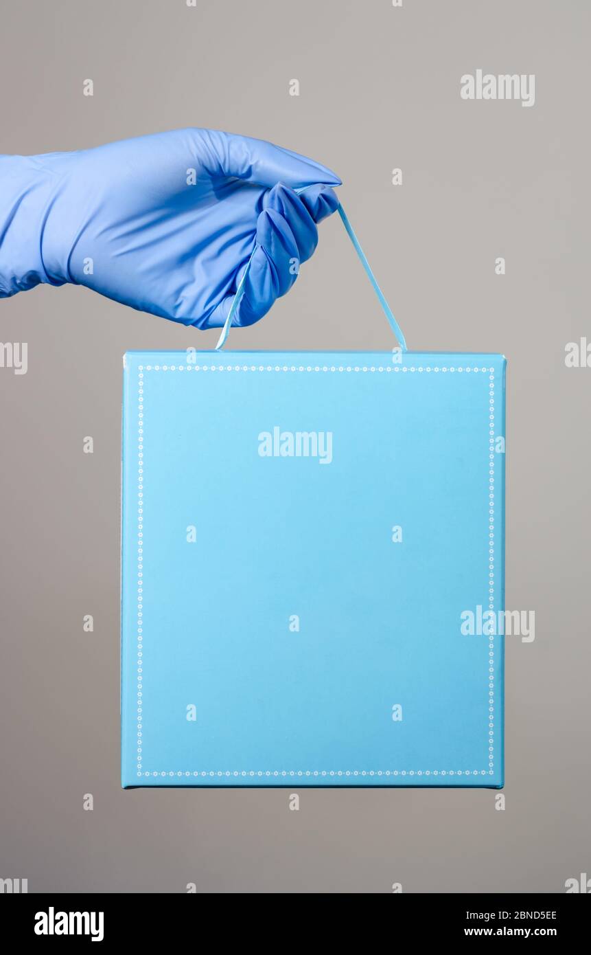 Hand mit chirurgischen Handschuhen einer Frau oder Mann mit einem blauen geschenkkarton Paket. Schutzmaßnahmen für die Verteilung von Paketen während der covi Stockfoto