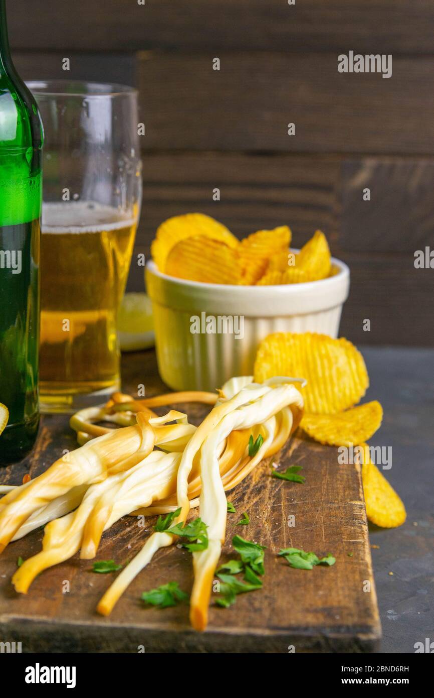 Käse mit Bier, Zitrone und Kartoffelchips auf dunklem Holzbrett. Snack auf Fisch mit Bier. Vorderansicht, Nahaufnahme Stockfoto