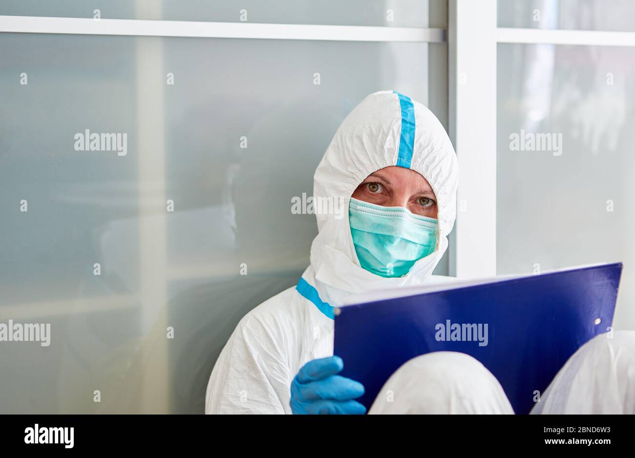 Pflegepersonal in der Klinik in Schutzkleidung mit Klemmbrett macht während der Coronavirus-Epidemie eine Pause auf dem Boden Stockfoto