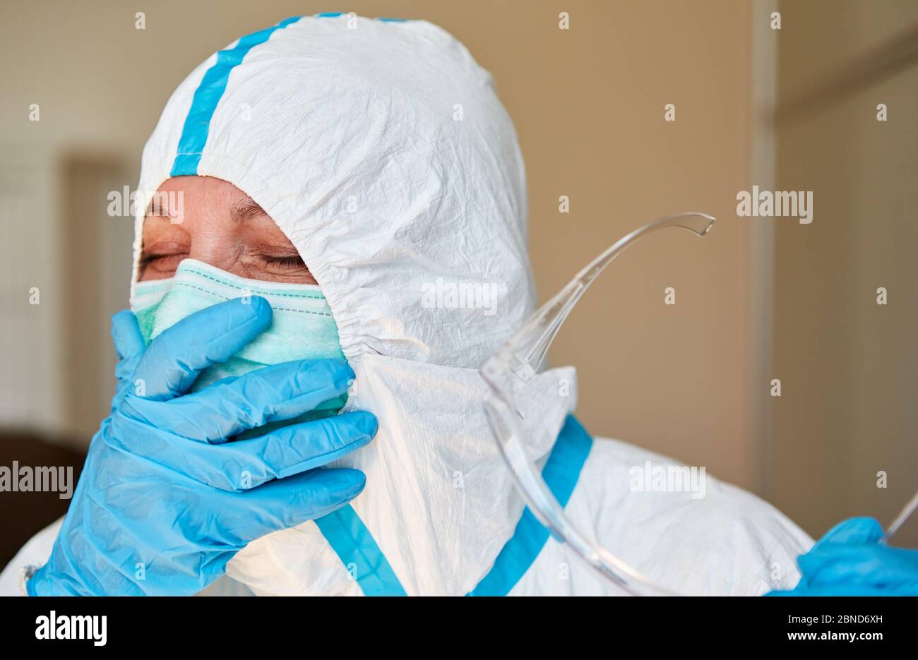 Müde Arzt in Schutzkleidung hält die Hand vor dem Gesicht, während in Coronavirus Pandemie Klinik gähnend Stockfoto