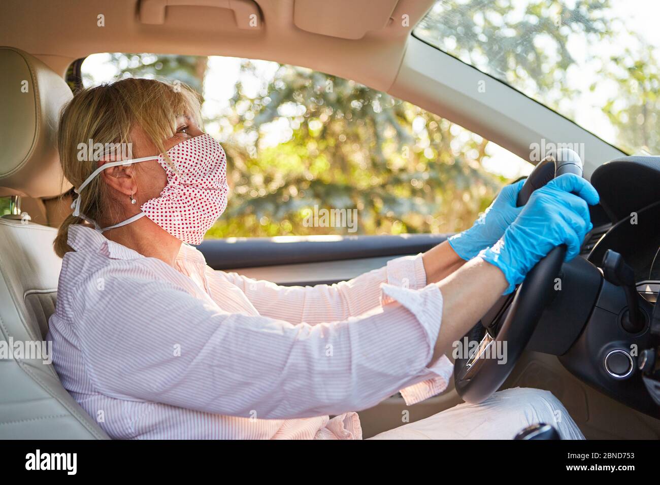 Ältere Frau mit Gesichtsmaske und Einweghandschuhen wegen einer Coronavirus-Pandemie während einer Autofahrt Stockfoto