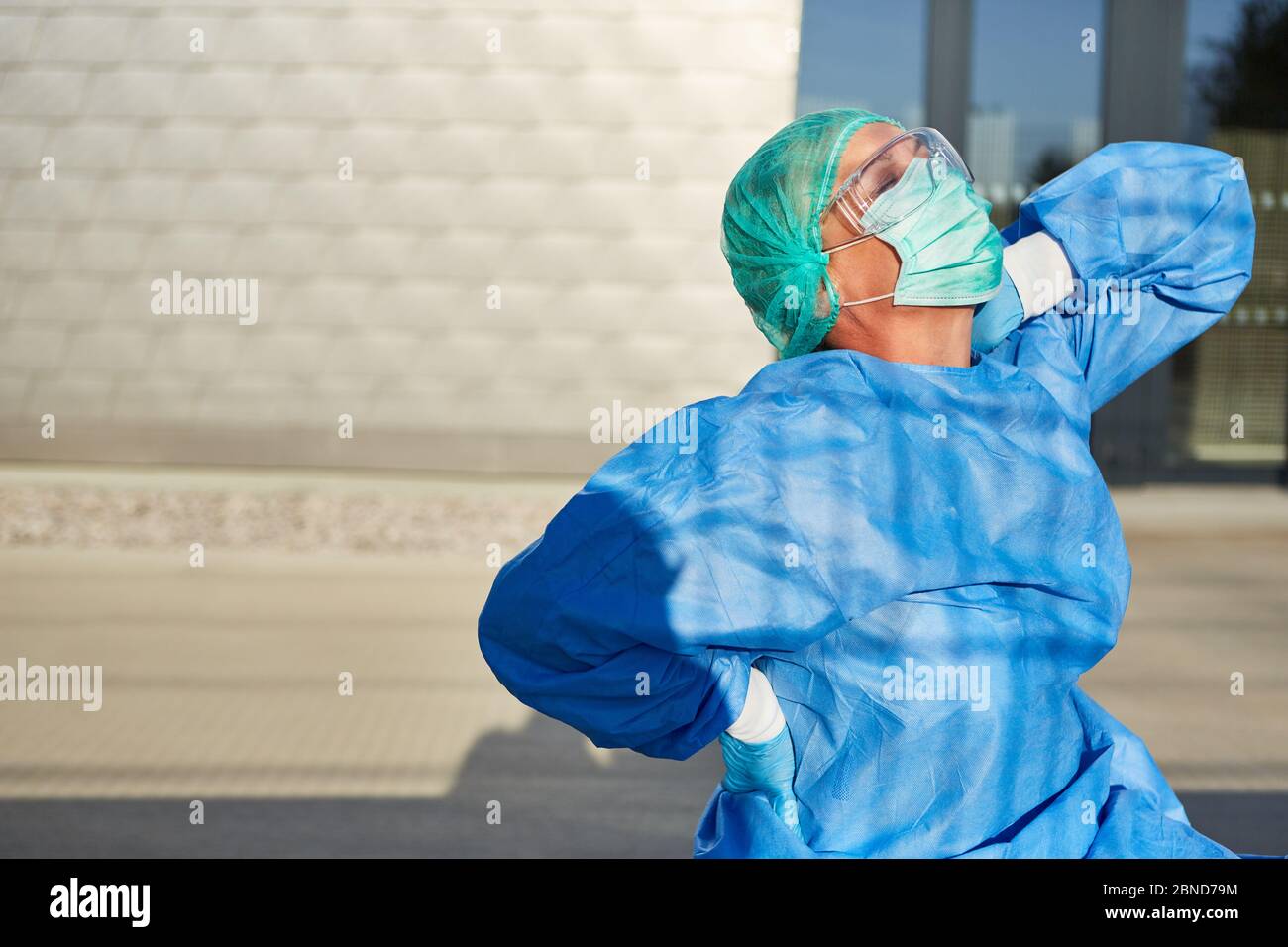 Ärztin mit Rückenschmerzen und Verspannungen vor der Klinik aufgrund von Stress und Überlastung bei der Coronavirus-Pandemie Stockfoto