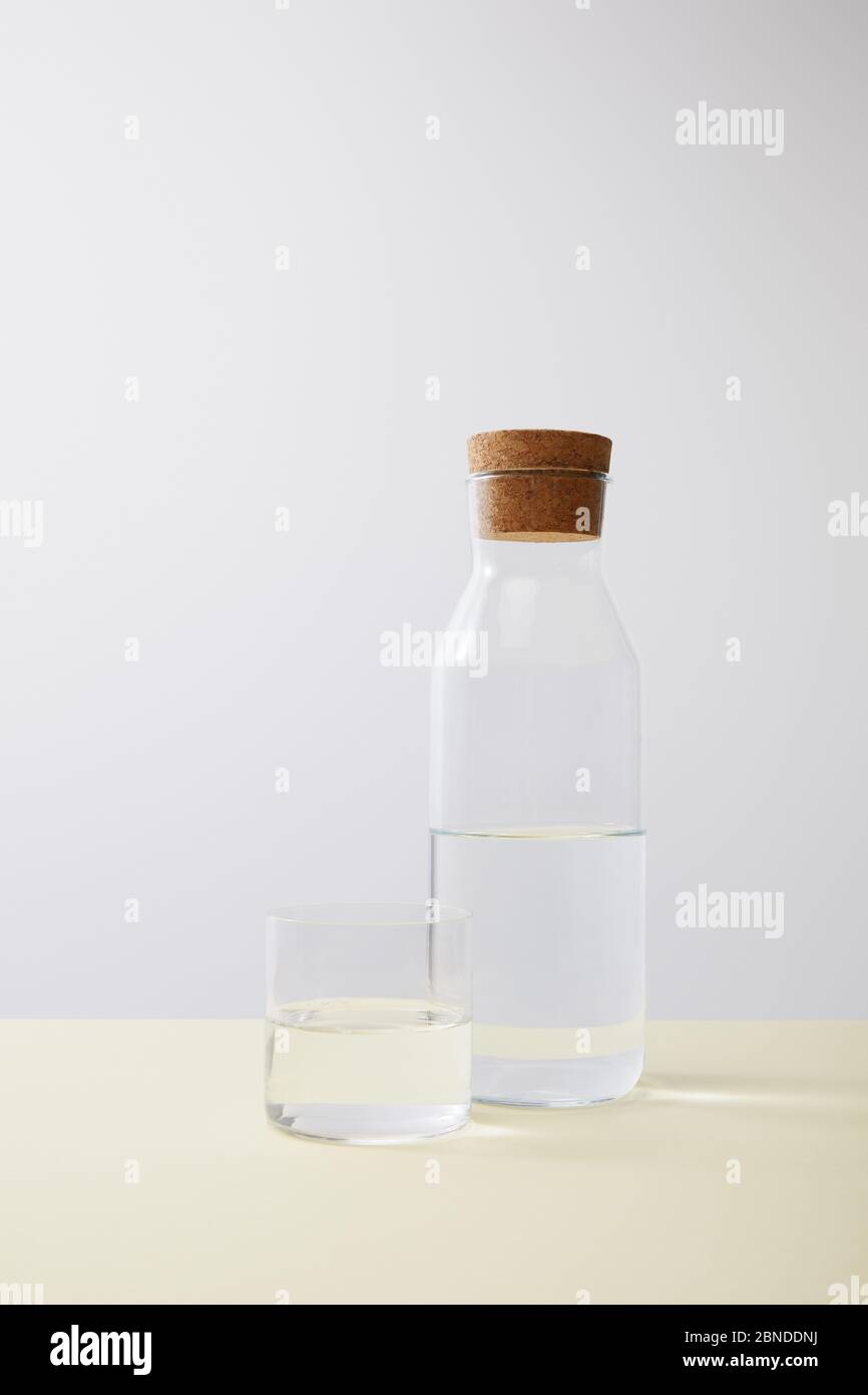 Flasche mit Kork und Glas mit Wasser auf isoliert auf grau gefüllt Stockfoto