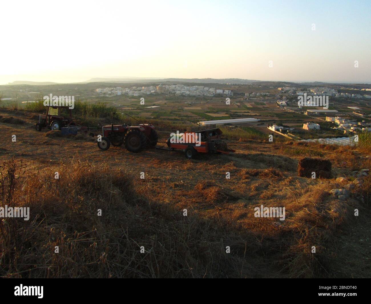 MGARR, MALTA - Jul 19, 2014: Ein Traktor oder Erntemaschine, landwirtschaftliche Fahrzeug, geparkt in einem Feld, nach dem Schneiden des Weizens und Stapeln für Heu. Landwirtschaft Stockfoto