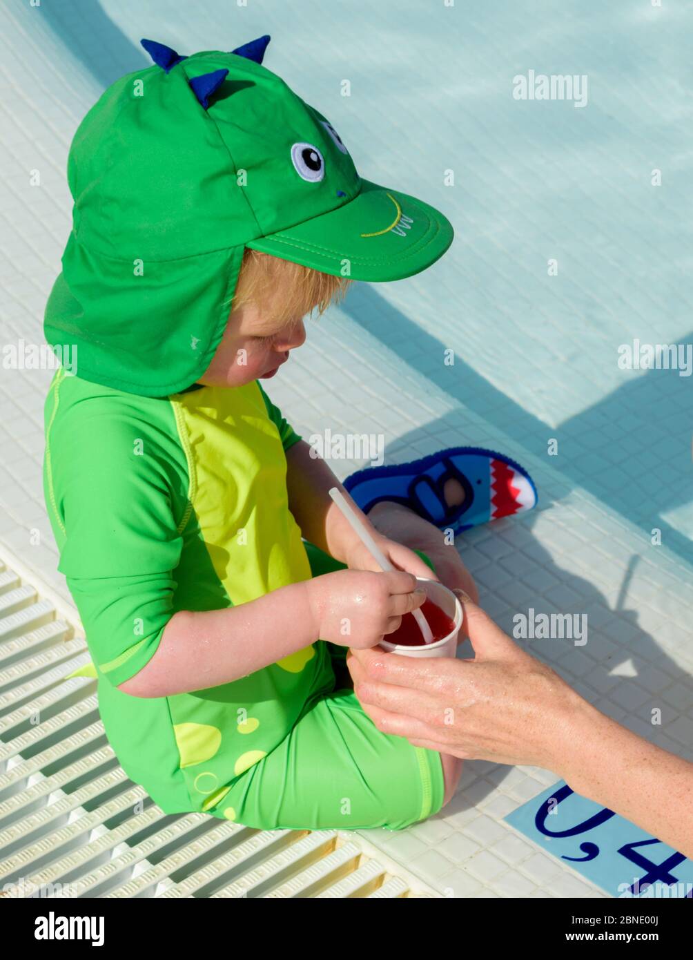 Ein kleines Kind wird ein kaltes Getränk gegeben, um während des Spielens im Pool an einem heißen Sommertag hydratisiert zu bleiben Stockfoto
