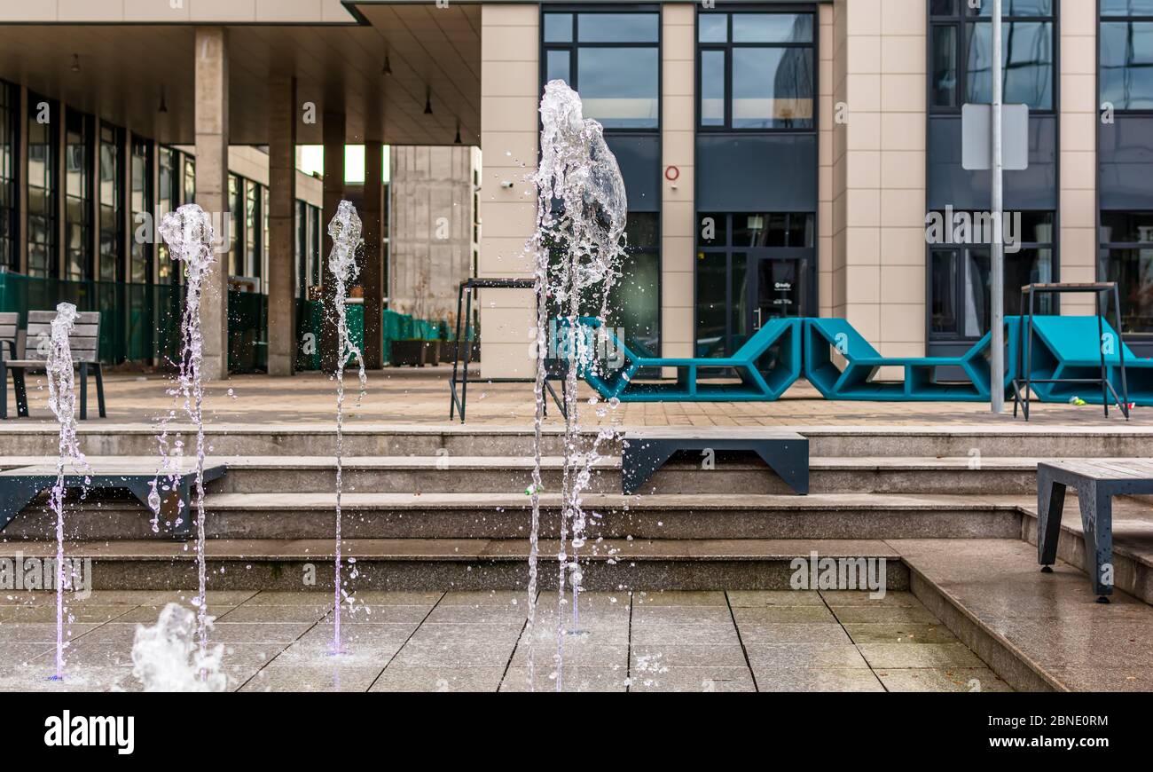 Tanzender Brunnen mit Bürogebäuden und schicken grünen Bänken. Brunnen befindet sich in riesigen Büro-und Wohnkomplex Jauna Teika (New Tale). Stockfoto