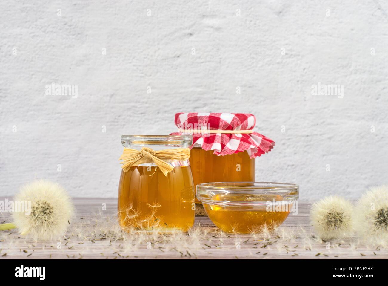 Löwenzahn-Marmelade, Honig, Gelee in einem Glasgefäß auf einem Holztisch, weißer Hintergrund mit frischen Blumen, Löwenzahn luftigen Samenköpfen, Samen, Blaskugeln Stockfoto