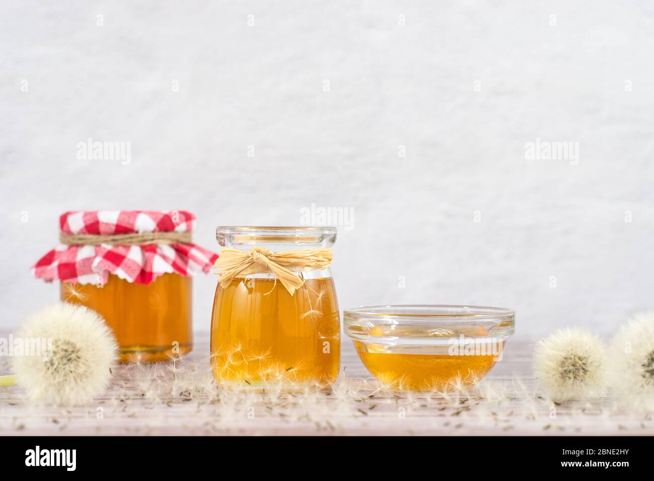 Löwenzahn-Marmelade, Honig, Gelee in einem Glasgefäß auf einem Holztisch, weißer Hintergrund mit frischen Blumen, Löwenzahn luftigen Samenköpfen, Samen, Blaskugeln Stockfoto