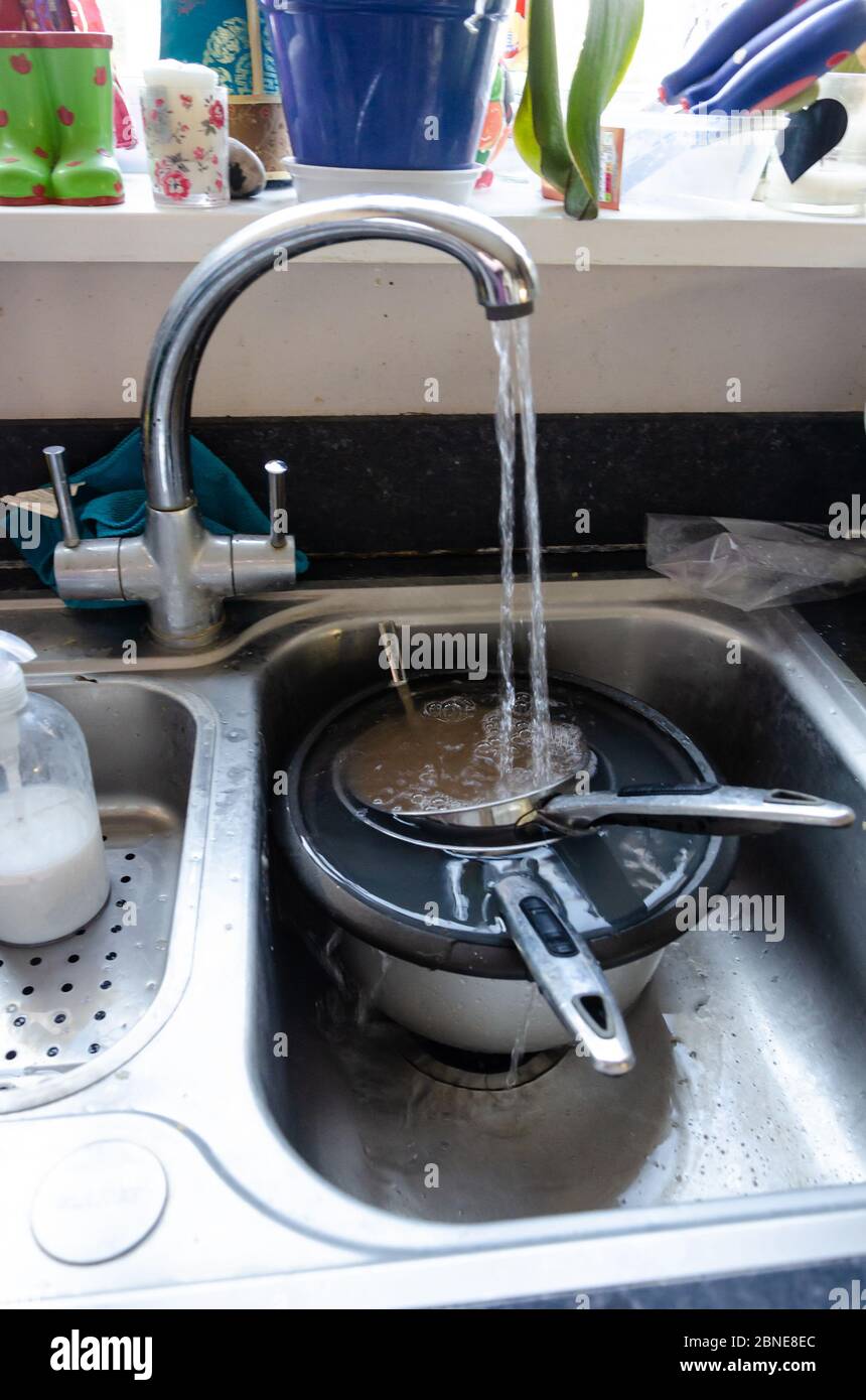 Ein fließendes Wasser füllt schmutzige Pfannen, damit sie in einer Spülbecken einweichen können, um sie leichter zu reinigen. Stockfoto