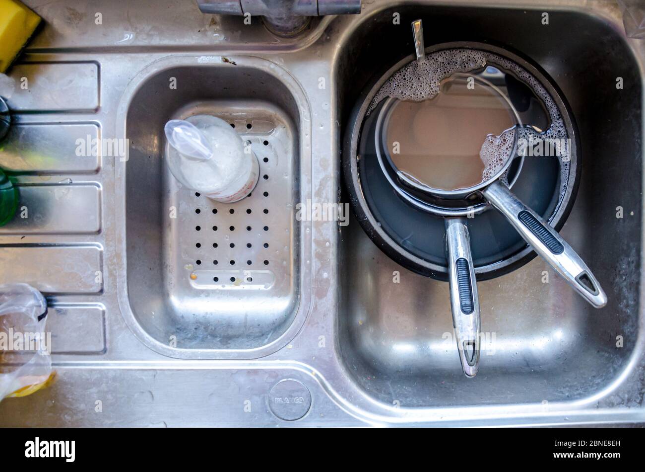 Schmutzige Pfannen voller Wasser, die in einem Spülbecken in der Küche einweichen, um sie leichter zu reinigen. Stockfoto