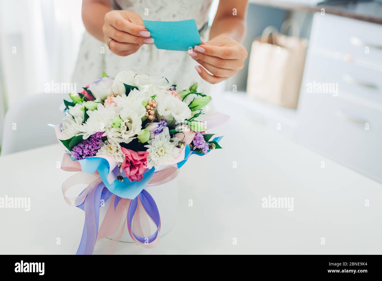 Frau liest Karte in Blumenstrauß von Freund in Geschenkbox auf der Küche zu Hause gelassen. Überraschungsgeschenk Stockfoto