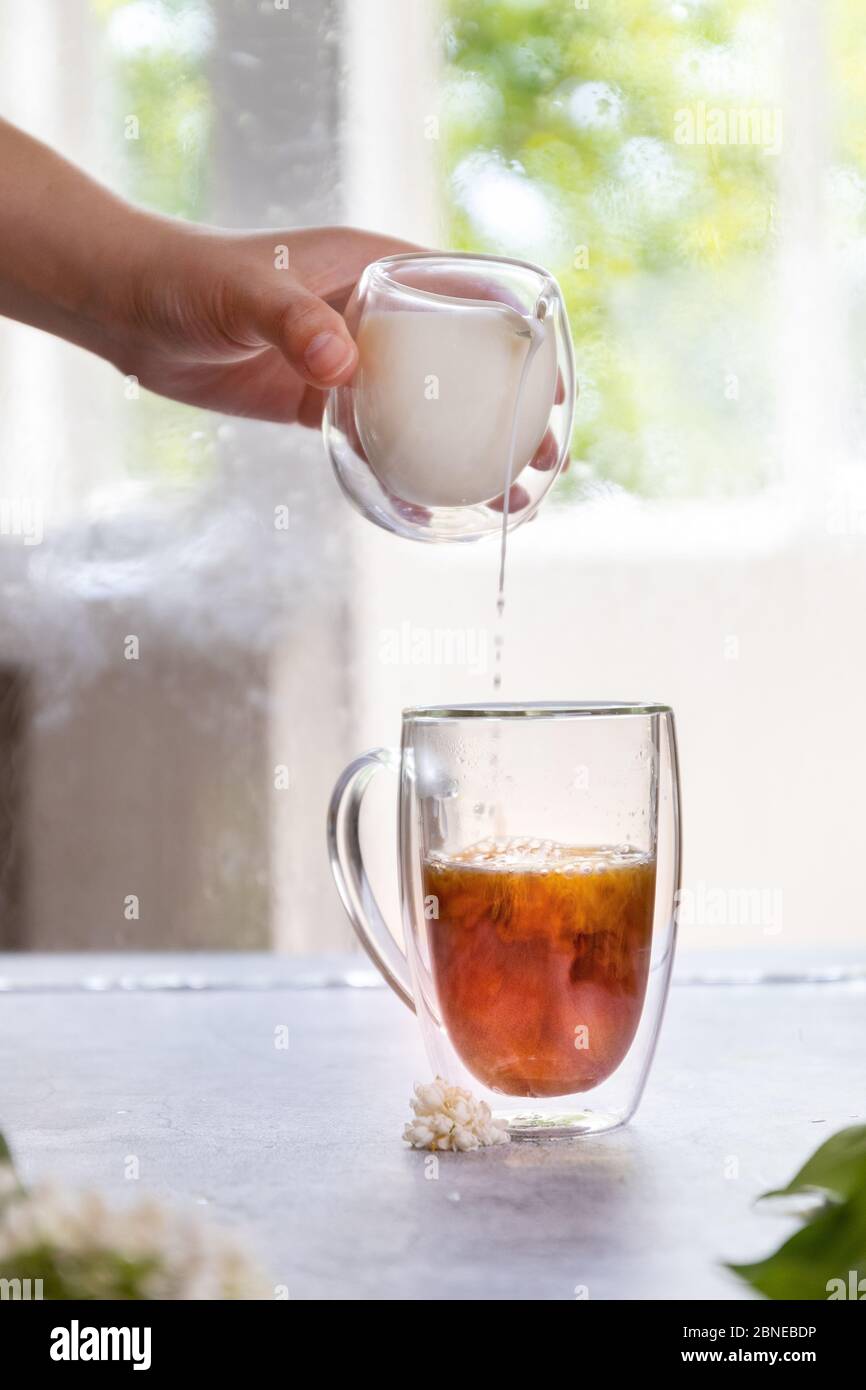 Nahaufnahme der weiblichen Hand, die Milch in Tee gießt, vertikales Foto Stockfoto