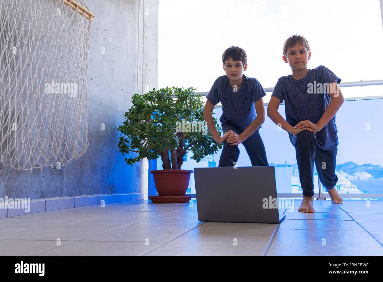 Kinder mit Laptop-Computer, die zu Hause auf dem Balkon Sportübungen machen. Sport, gesunder Lebensstil, aktive Freizeit, Online-Training zu Hause Stockfoto