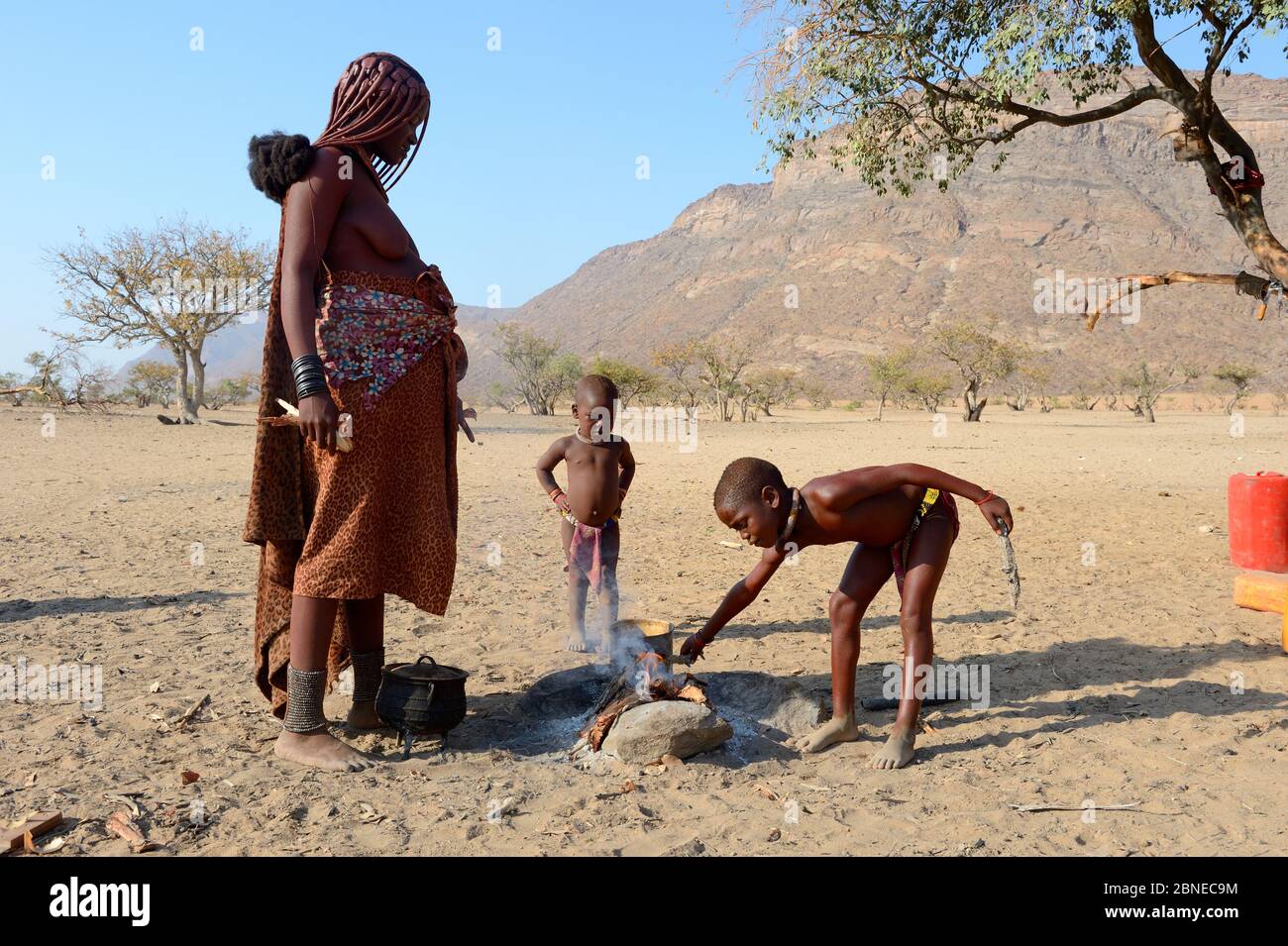 Himba Mädchen Feuer mit ihrer Mutter für die Küche, Marienfluss Valley, Kaokoland Wüste, Namibia. Oktober 2015 Stockfoto