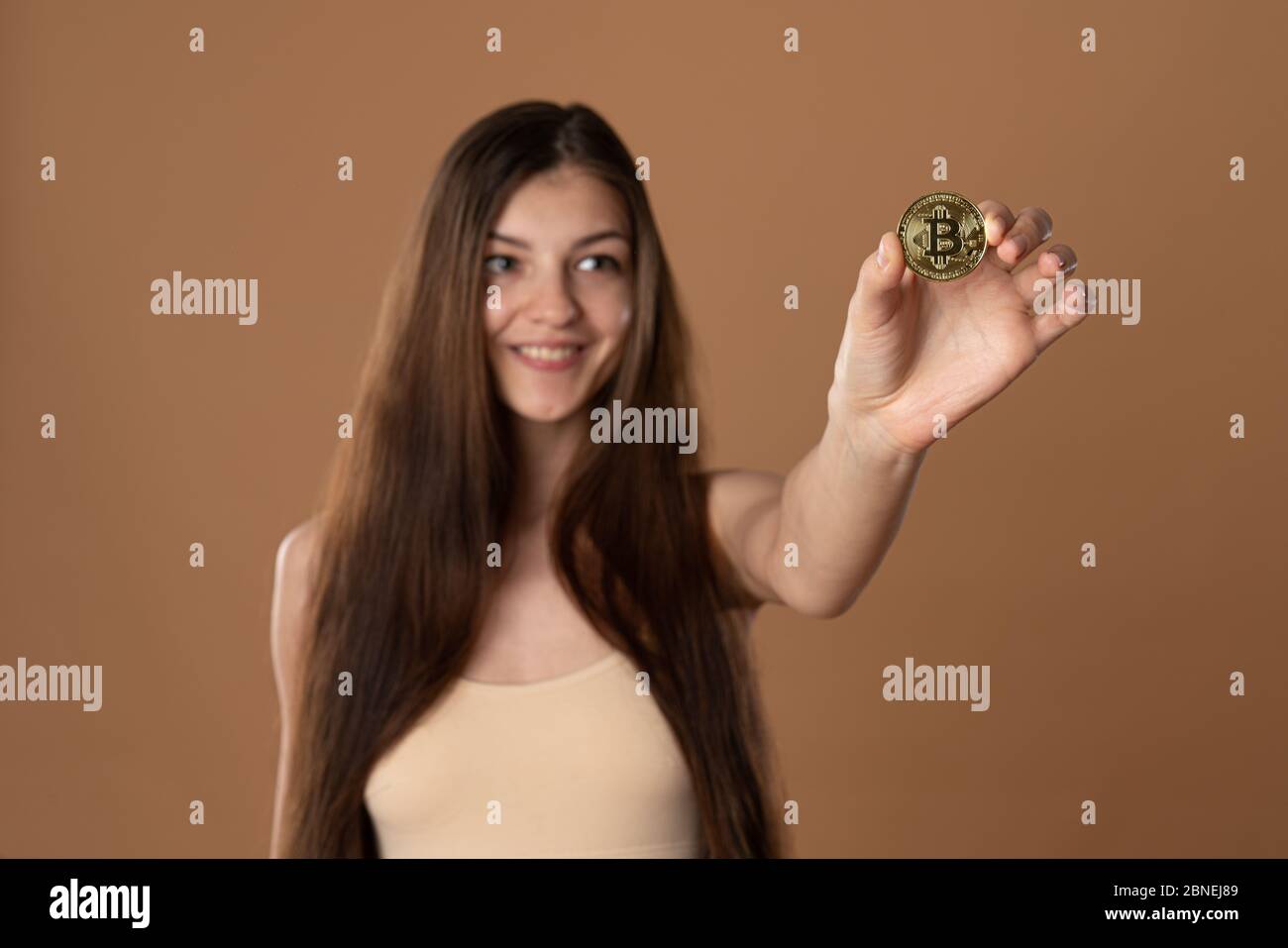 Glücklich Mädchen Eith Brünette verlieren Haare hält Bitcoin goldene Münze in der Hand, konzentrieren sich auf die Münze, Mädchen ist verschwommen Stockfoto