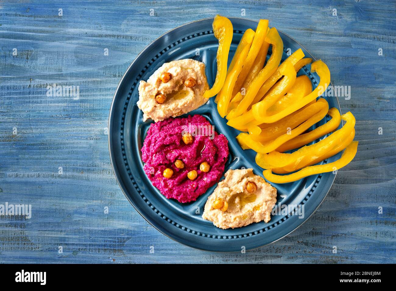 Nahaufnahme bunte blaue Platte mit gelben Paprikapulzen und roten Rüben Hummus Dip Stockfoto
