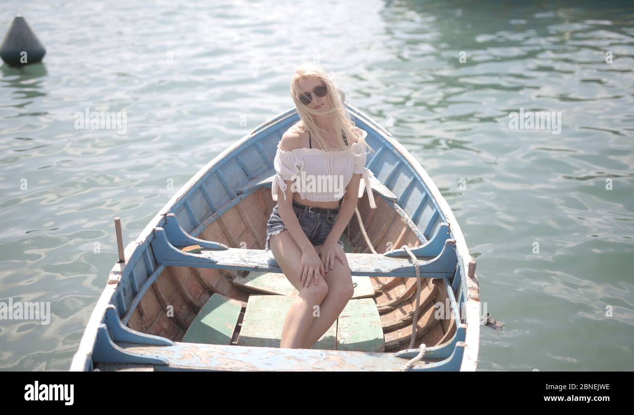 Junge blonde Frau sitzt in einem Holzboot auf dem Wasser unter dem Sonnenlicht am Tag Stockfoto