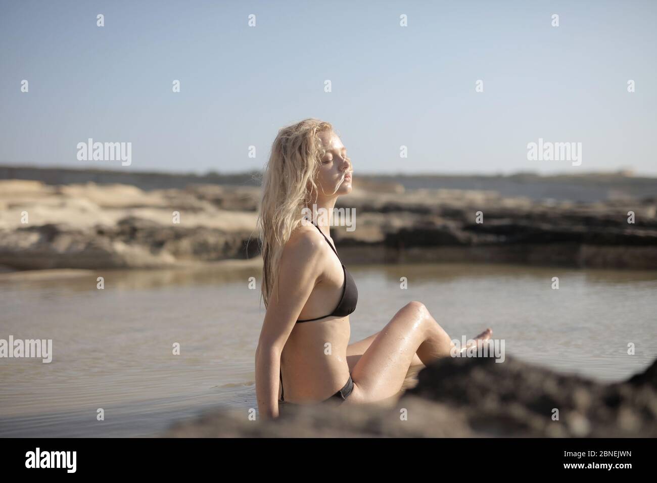 Junge blonde Frau posiert im Meer von Felsen umgeben Bei Tageslicht Stockfoto