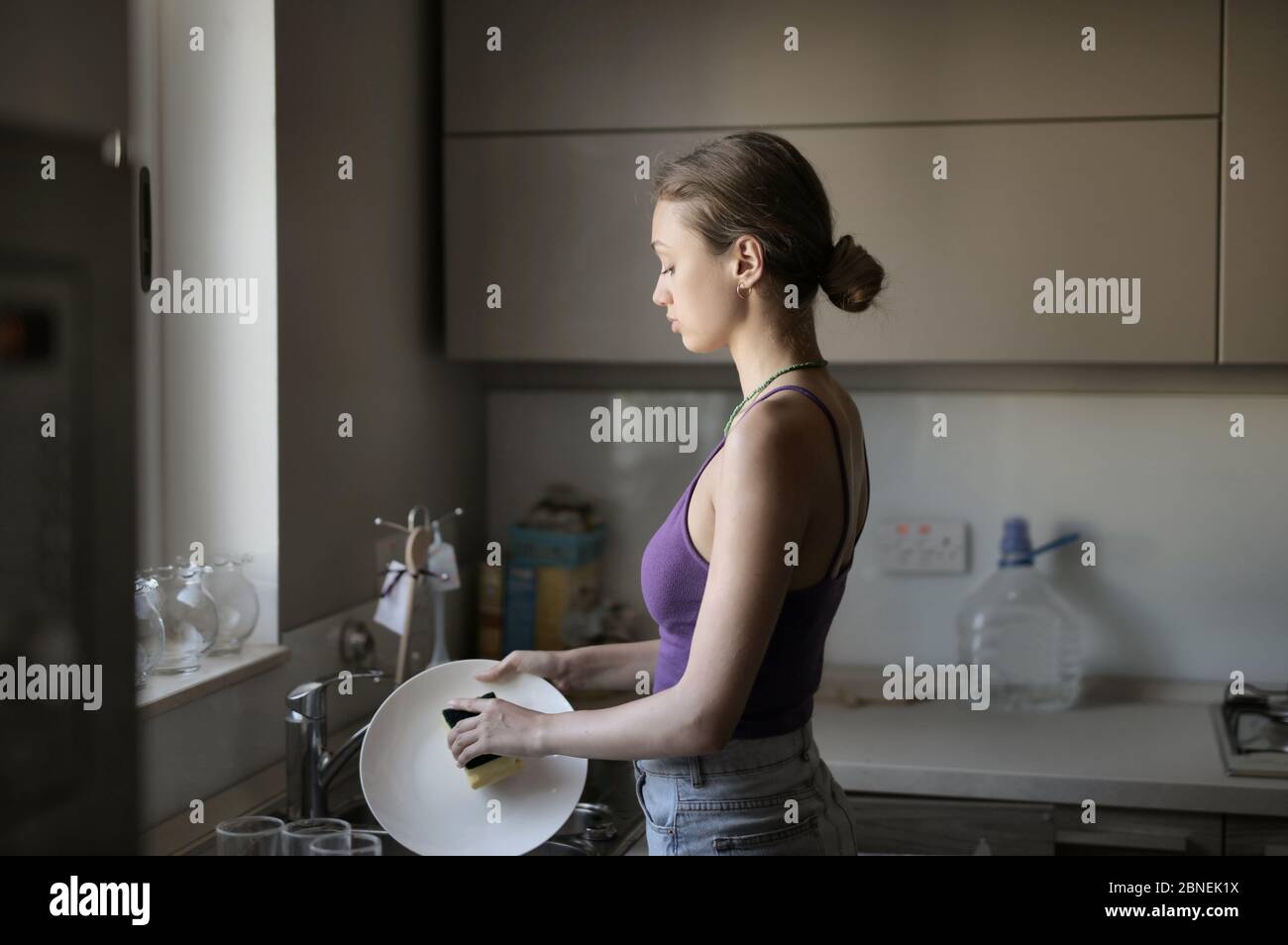 Junge Frau, die das Geschirr in der Küche unter dem Leuchtet Stockfoto