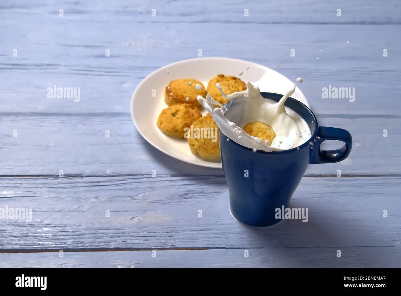 Cookie mit Milchspritzer in blauer Tasse auf hellblauem Holzhintergrund. Stockfoto