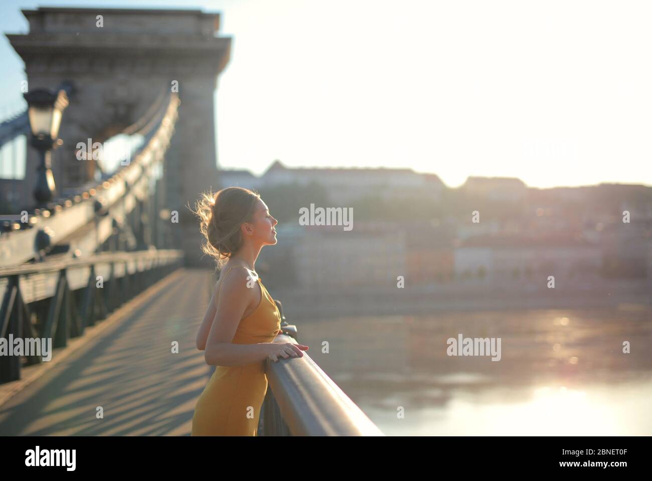 Junge Frau in gelbem Kleid auf dem Szechenyi Kettenbrücke unter dem Sonnenlicht in Ungarn Stockfoto
