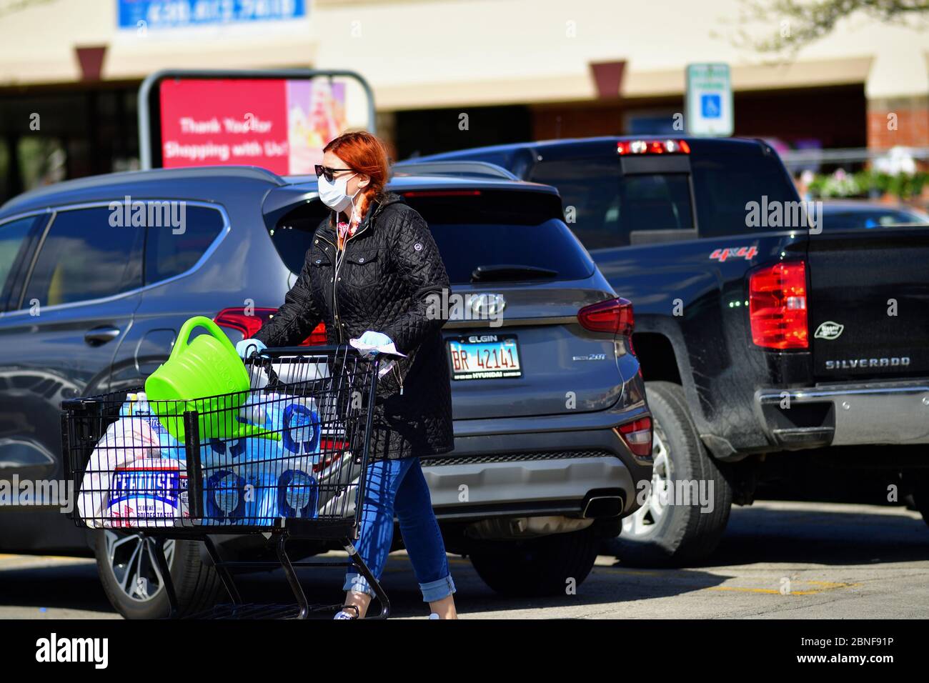 Carol Stream, Illinois, USA. Shopper ausgestattet mit einer chirurgischen Maske und Handschuhen, nachdem sie aus einem Lebensmittelgeschäft auf dem Weg zu ihrem Fahrzeug. Stockfoto