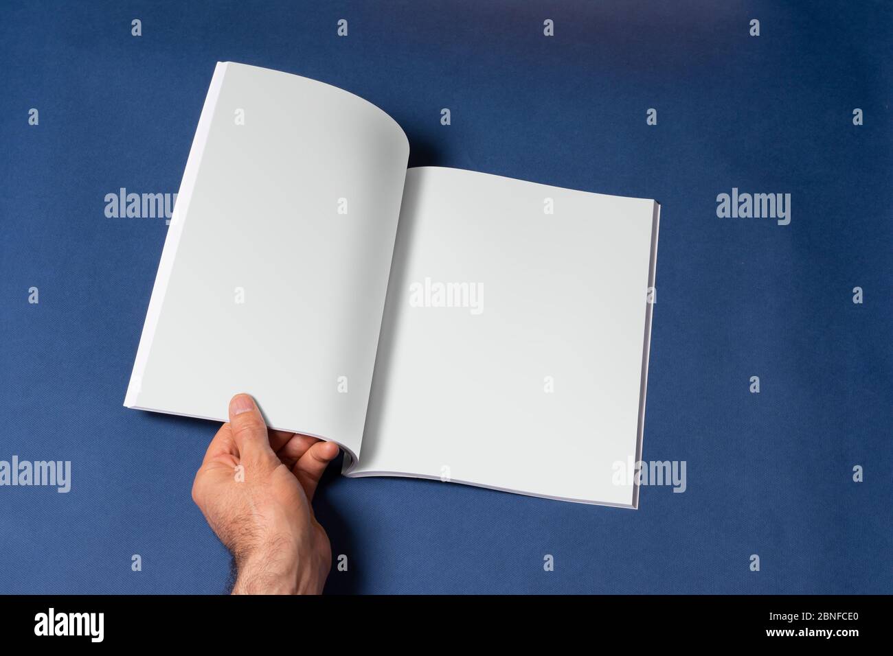 Männliche Hand öffnete einen Buch-Katalog auf blauem Hintergrund, Mock-up-Serie Vorlage bereit für Ihr Design, Seiten Auswahl Pfad enthalten Stockfoto