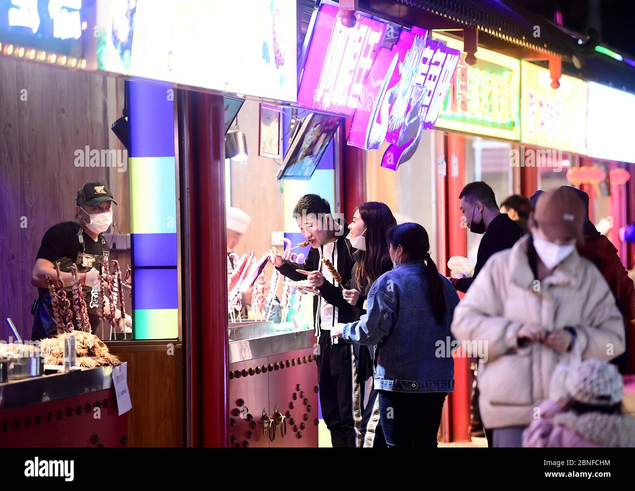 Die Kunden genießen Essen und schlendern durch die Snack Bars, wo der Besitzer auf dem Xingshun International Night Market, dem größten seiner Art in Asien, kocht Stockfoto