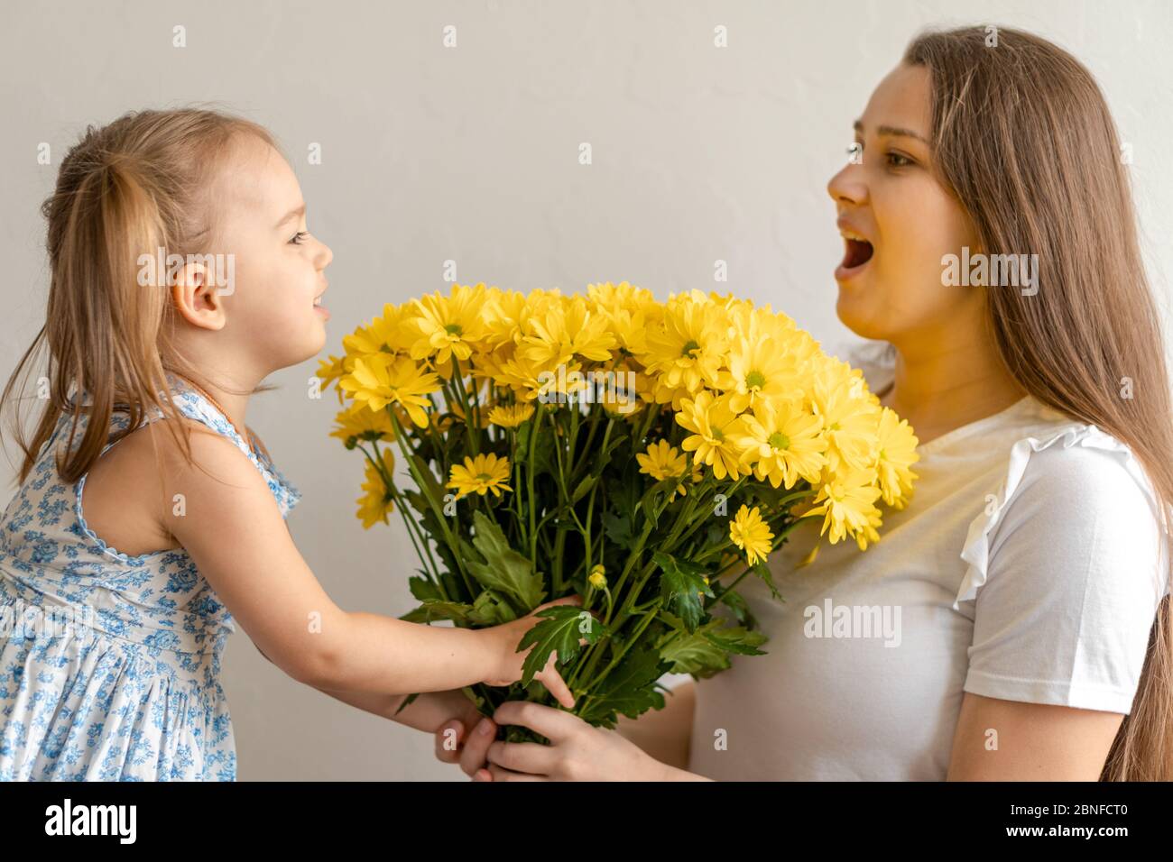 Mutterschaft, Muttertag, Geburtstag, Kindheit, Familienkonzept - close-up kleines Mädchen in blau bunten Kleid gratulieren und geben junge Mutter hell Stockfoto