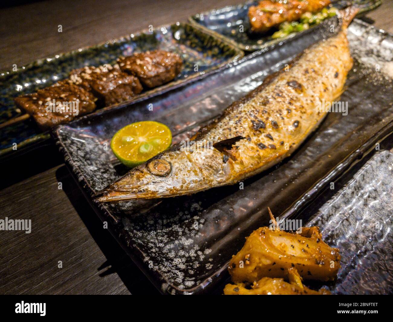 Ein Set köstlicher traditioneller Spieße vom Grill und ein Fisch zum Abendessen. Beliebte japanische Küche mit vielfältiger Auswahl im Restaurant. Appetitlich Japan Spießteller auf Stockfoto