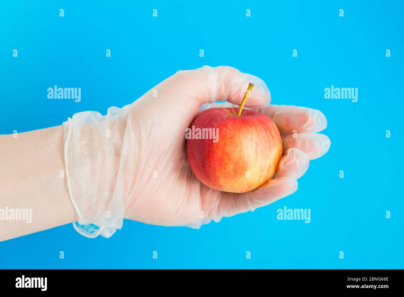 Hand in Gummihandschuh hält den roten Apfel. Konzeption der sicheren Lieferung Stockfoto