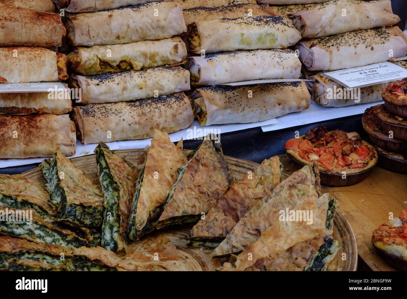 Anzeige von Spinat und Käseburk und Thai Curry Rollen zum Verkauf auf dem Freiluftmarkt. Portobello Road, Notting Hill, West London, England, Großbritannien. Stockfoto