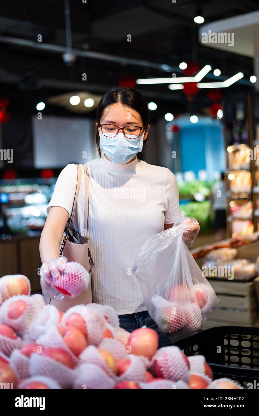 Asiatische Frau, die auf dem Markt nach Obst kauft, trägt Maske und Handschuhe, um die Ausbreitung des Virus während der Coronavirus-Pandemie zu verhindern Stockfoto