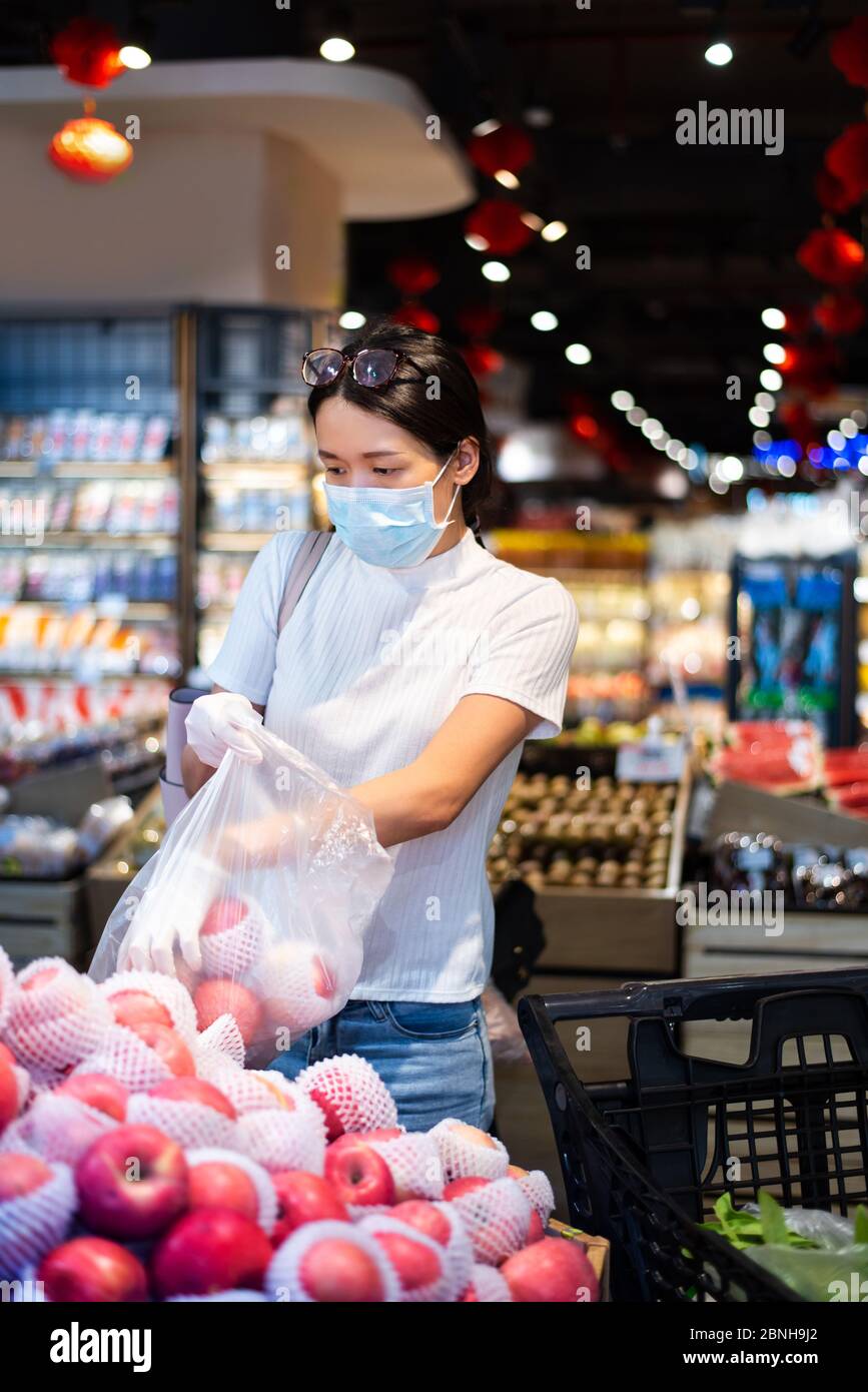 Asiatische Frau, die auf dem Markt nach Obst kauft, trägt Maske und Handschuhe, um die Ausbreitung des Virus während der Coronavirus-Pandemie zu verhindern Stockfoto