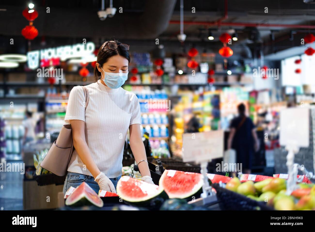 Asiatische Frau, die auf dem Markt nach Früchten kauft, trägt Maske und Handschuhe, um die Ausbreitung des Virus während der Coronavirus-Pandemie zu verhindern Stockfoto