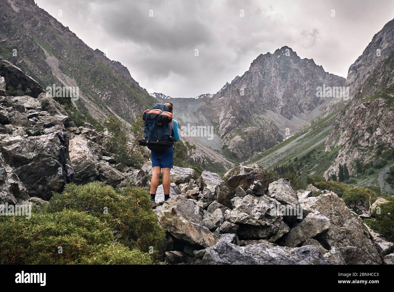 Tourist mit großem Rucksack ist auf dem felsigen Weg im Bergtal des Karakol-Nationalparks, Kirgisistan Stockfoto