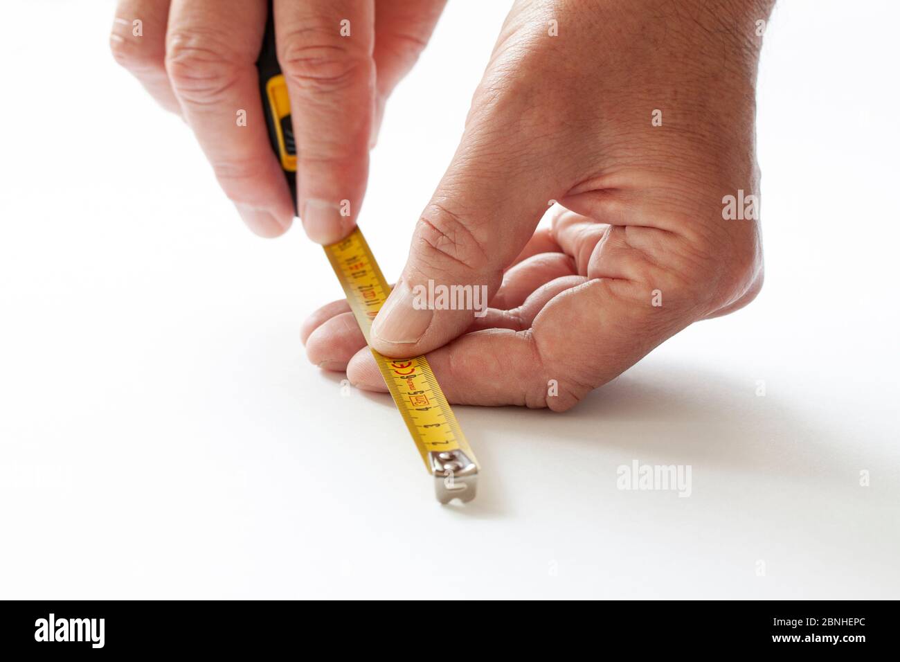 Mann, der mit Maßband arbeitet. Nahaufnahme der Hände, die Mesure-Band auf weißem Hintergrund halten. Stockfoto