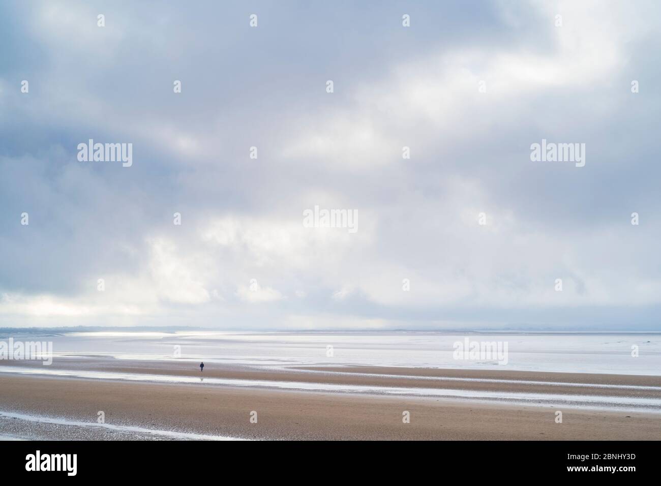Einsame Figur beim Spaziergang am Sandstrand und genießen die Einsamkeit entlang der Küste am Bristol Channel in Burnham-on-Sea Seaside, Somerset, Großbritannien Stockfoto
