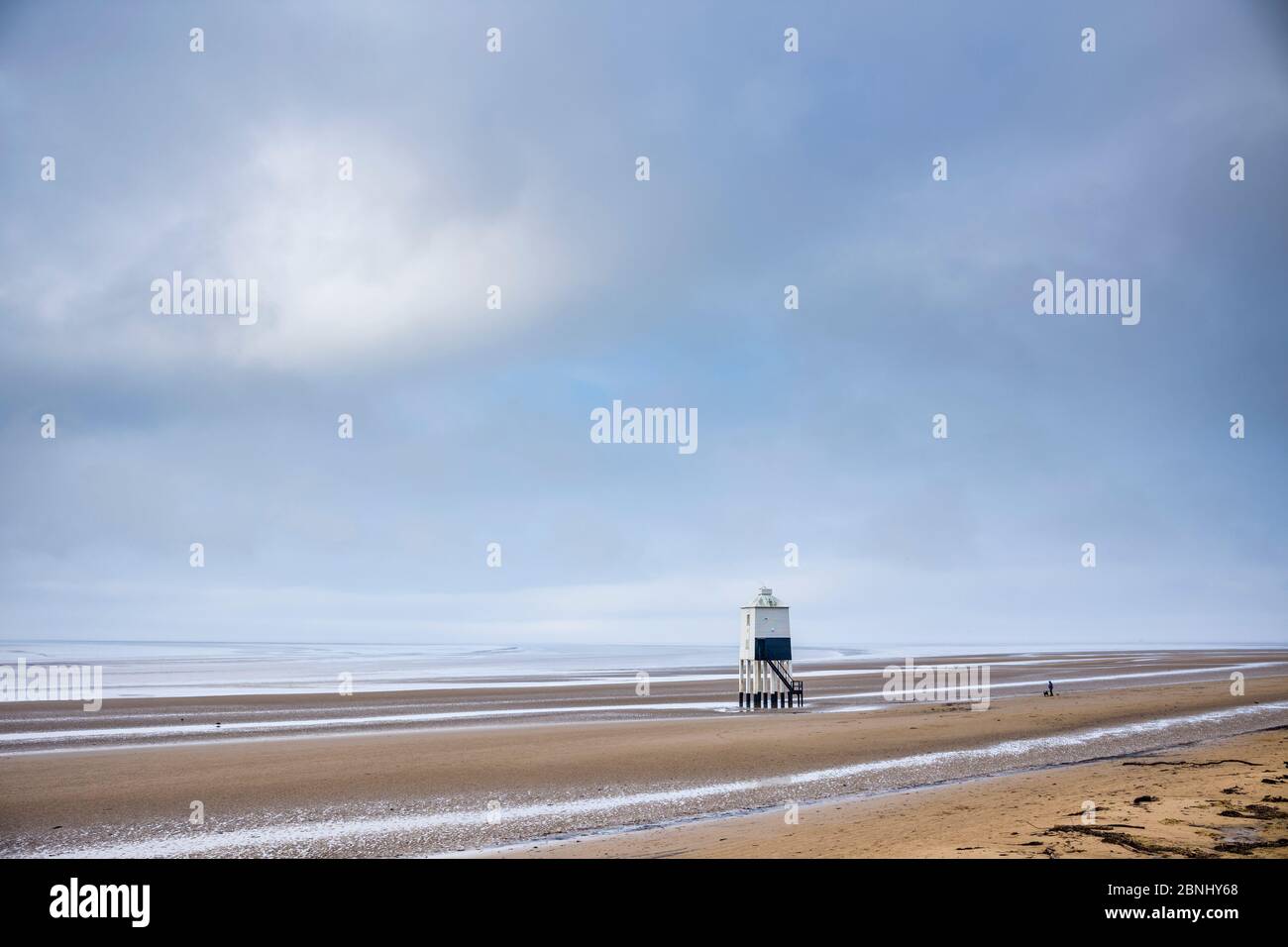 Eine Person, die Hunde entlang des Sandstrandes der Küste entlang läuft und die Einsamkeit am Bristol Channel in Burnham-on-Sea, Somerset, Großbritannien, genießt Stockfoto