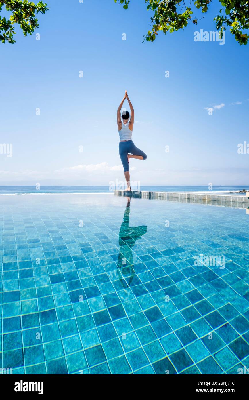 Eine junge Frau, die Yoga neben einem Infinity-Pool praktiziert, Candidasa, Bali, Indonesien, Südostasien, Asien Stockfoto