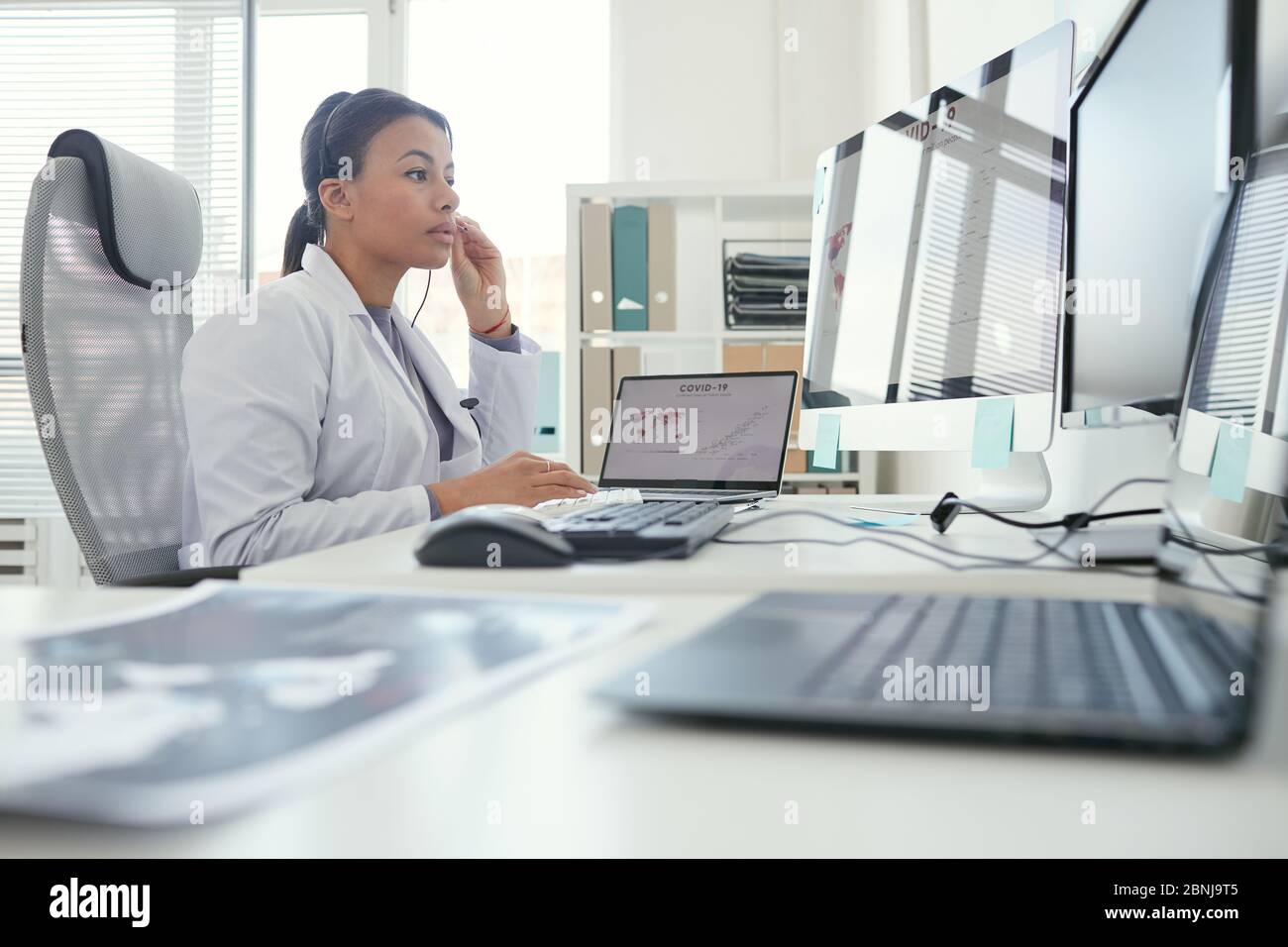 Seriöse Ärztin in Kopfhörer Blick auf Computer-Monitor hat sie Online-Konferenz im Büro Stockfoto
